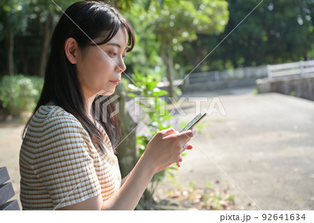 公園のベンチでスマホを操作する女性 92641634