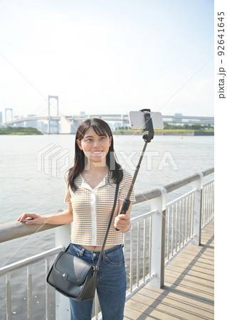 海辺で自撮り棒を使ってスマホで撮影をする女性 海辺で自撮り棒を使ってスマホで撮影をする女性 92641645