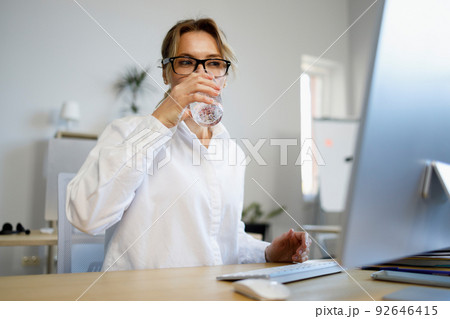 Beautiful mature business woman working at a computer and drinking glass of fresh water Beautiful mature business woman working at a computer and drinking glass of fresh water 92646415