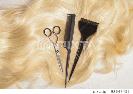 Hairdresser's scissors with comb on strand of blonde hair background, top view 92647435