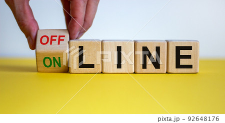 Hand turns a cube and changes the word 'offline' to 'online' or vice versa. Beautiful yellow table, white background. Business concept. Copy space. 92648176