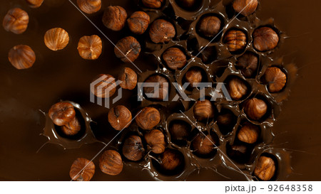 Super Slow Motion of Falling Hazelnuts into Dark Hot Melted Chocolate, Close-up, Top Shot. 92648358