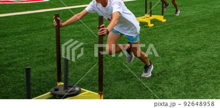 Runners pushing sleds with weights on a turf field Runners pushing sleds with weights on a turf field 92648958