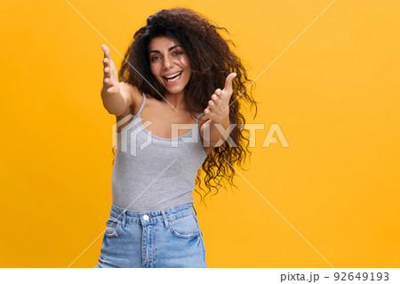 NICE TO MEET YOU. FRIENDLY HUGS CONCEPT. Enjoyed pretty Latin female with afro reach for camera, smile to you, stay isolated over yellow background. Copy space, free place NICE TO MEET YOU. FRIENDLY HUGS CONCEPT. Enjoyed pretty Latin female with afro reach for camera, smile to you, stay isolated over yellow background. Copy space, free place 92649193