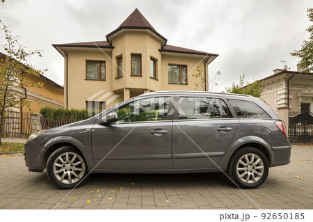 New expensive gray car parked in paved parking lot in front of big two story cottage. Luxury and prosperity concept. New expensive gray car parked in paved parking lot in front of big two story cottage. Luxury and prosperity concept. 92650185