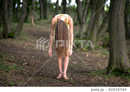 Creepy woman with long hair standing bent down in moody dark forest. Creepy woman with long hair standing bent down in moody dark forest. 92650594