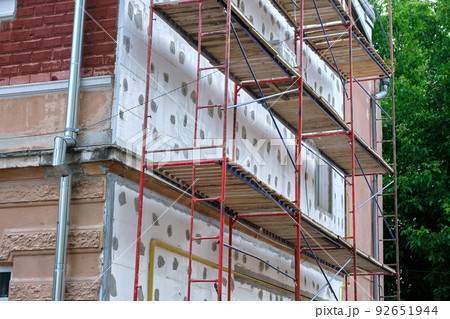 Building facade under renovation works with construction scaffolding frame. Wall insulation with styrofoam sheets for energy efficient home 92651944