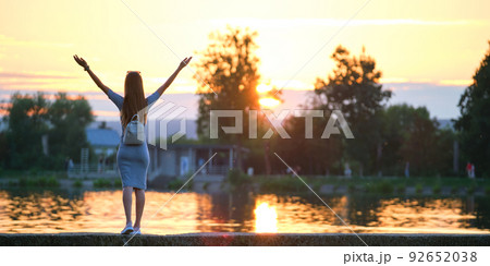 Back view of lonely woman standing on lake side with outstretched hands on warm summer evening. Success and vitality concept. Back view of lonely woman standing on lake side with outstretched hands on warm summer evening. Success and vitality concept. 92652038