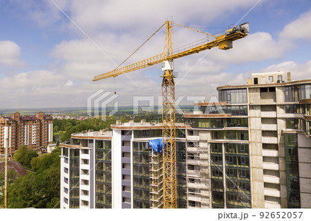 Apartment or office tall building under construction. Brick walls, glass windows, scaffolding and concrete support pillars. Tower crane on bright blue sky copy space background. 92652057