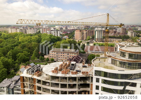 Apartment or office tall building under construction. Brick walls, glass windows, scaffolding and concrete support pillars. Tower crane on bright blue sky copy space background. 92652058
