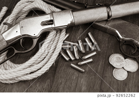 Old west gun - lever-action repeating rifles with ammunition and silver dollar coins. Sepia tone. Old west gun - lever-action repeating rifles with ammunition and silver dollar coins. Sepia tone. 92652262