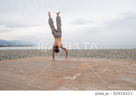 Shirtless caucasian man doing backflip on pebble beach. Shirtless caucasian man doing backflip on pebble beach. 92658321