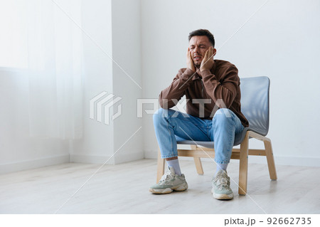 Sleepy tired upset unhappy young man touch head both hands closes eyes suffering from headache migraine sleeplessness sitting on chair at home. Mental problems Depression concept. Copy space Sleepy tired upset unhappy young man touch head both hands closes eyes suffering from headache migraine sleeplessness sitting on chair at home. Mental problems Depression concept. Copy space 92662735