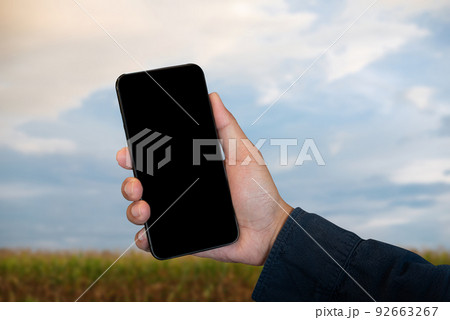 Mockup image of hand holding blank mobile phone with blank white screen in field, panorama with copy space. Mockup image of hand holding blank mobile phone with blank white screen in field, panorama with copy space. 92663267