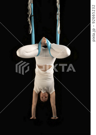 Girl practices fly yoga. Young woman upside down during an aerial gymnastics exercise. Isolated on black background. 92665232