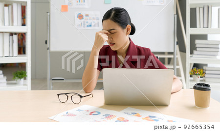Young asian businesswoman massages between eyes with fingers. The concept of unemployed, sadness, depressed and human problems. 92665354