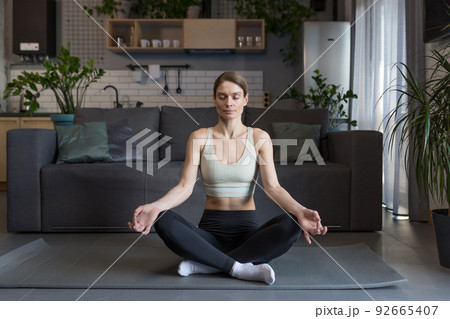 Woman at home sitting on the floor in the lotus position, meditating 92665407