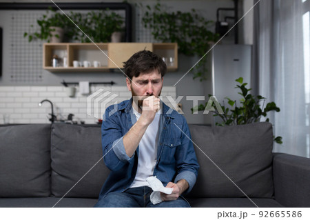 Sick man at home, patient coughing sitting on sofa in kitchen 92665586