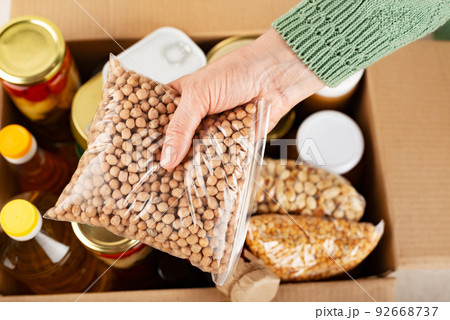 Plastic container with chickpeas in female hand on emergency food box background 92668737