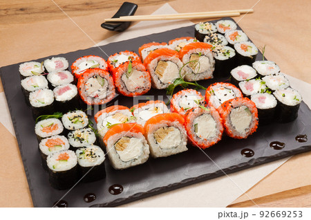 a large set of sushi rolls on a black stone plate 92669253
