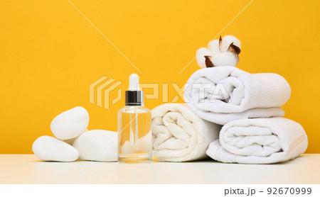 Glass bottle with a pipette and twisted white terry towels on the table Glass bottle with a pipette and twisted white terry towels on the table 92670999