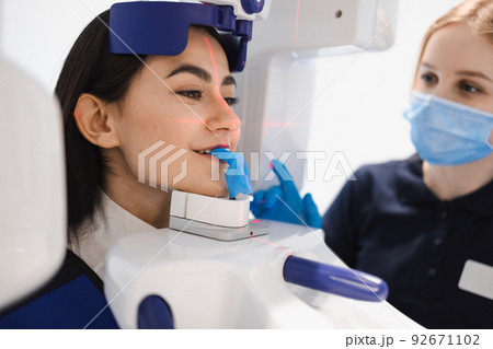 Female patient make a dental computer tomograph. The radiologist makes a CT scan of the jaw. Woman taking panoramic x-ray of teeth in clinic 92671102