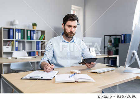 Portrait of a young man. Accountant, economist, financier. Counts on a calculator, sits at a desk at the computer, works with documents 92672696