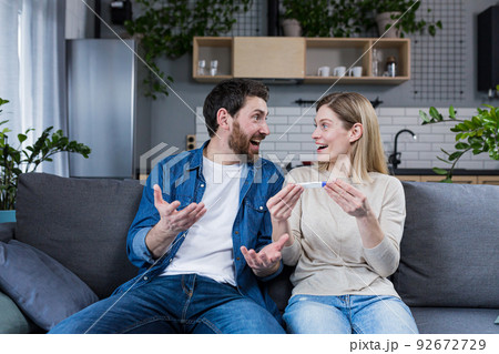 Young family enjoys a positive pregnancy test, a happy man and woman sit on the couch and hug Young family enjoys a positive pregnancy test, a happy man and woman sit on the couch and hug 92672729