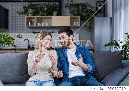 Happy couple man and woman on the couch sitting and rejoicing in a positive pregnancy test Happy couple man and woman on the couch sitting and rejoicing in a positive pregnancy test 92672730
