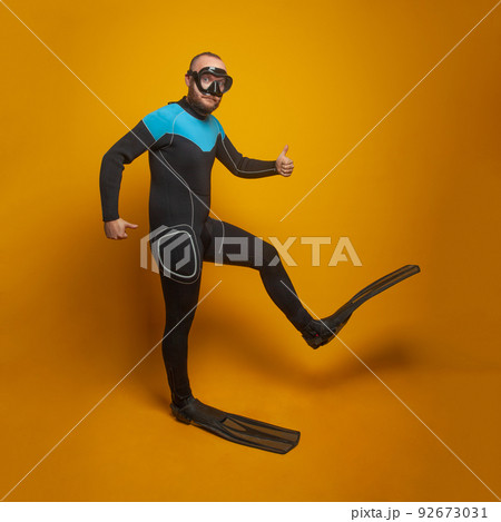 Happy scuba diver diving man going to the side against bright orange studio wall background Happy scuba diver diving man going to the side against bright orange studio wall background 92673031