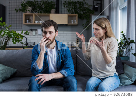 Family quarrel, man and woman sitting on sofa at home. angry woman yells at her husband, blames. The man is silent. He listens, holds his head, embarrassed 92673088