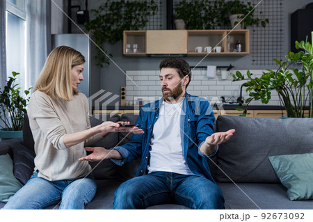 A woman quarrels with her husband, the claim of a lazy man who earns little money, a married couple quarrels sitting on the couch 92673092