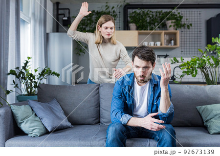 Family quarrel, woman quarrels and yells at the loser's husband, couple at home sitting in the living room on the couch Family quarrel, woman quarrels and yells at the loser's husband, couple at home sitting in the living room on the couch 92673139