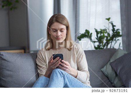 Beautiful middle-aged woman sitting on the couch at home, using the phone and smiling 92673191