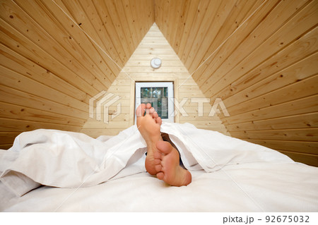 Legs of woman stick out from under the blanket Legs of woman stick out from under the blanket 92675032