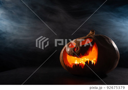 A creepy pumpkin with a carved grimace in the smoke. Jack o lantern in the dark. 92675379