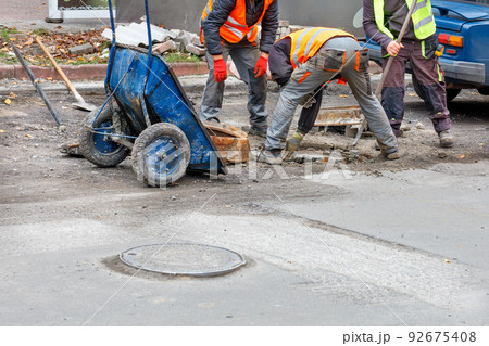 A team of road workers are repairing a sewer manhole on the carriageway. 92675408