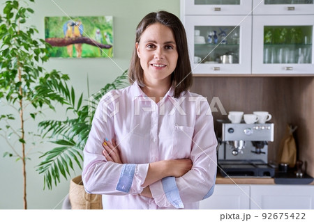 Portrait of young woman looking at camera in kitchen Portrait of young woman looking at camera in kitchen 92675422