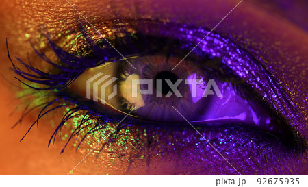 Close-up of woman eye under neon light. Female with beautiful makeup, glitter shadows. Beauty Close-up of woman eye under neon light. Female with beautiful makeup, glitter shadows. Beauty 92675935