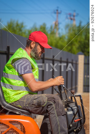 A man on a mini-excavator levels a piece of land, loosens the soil. 92676024