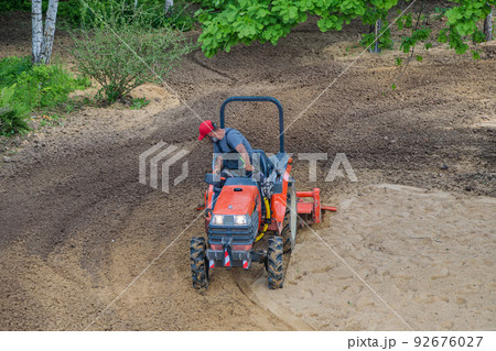 A farmer on a mini tractor loosens the soil for the lawn. Land cultivation, surface leveling 92676027