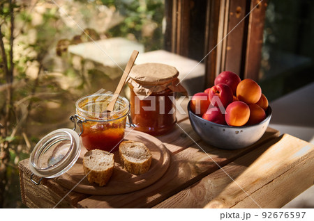 Still life. Homemade jam in jar, slices of freshly baked bread and sweet ripe organic apricots against a wooden window 92676597