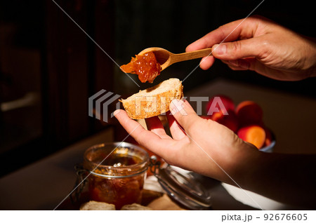 Food and drink, summer autumn harvest concept. Cropped view of the hands of a housewife spreading apricot jam on bread 92676605
