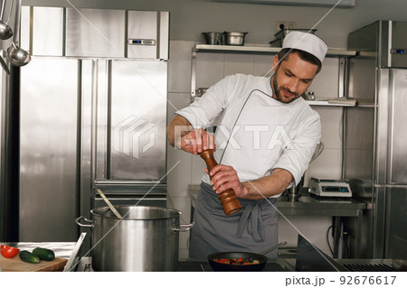 Chef adding salt or pepper to dish while cooking on restaurant kitchen 92676617