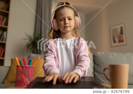Displeased Schoolgirl Using Laptop Wearing Headphones Learning Online At Home 92676706