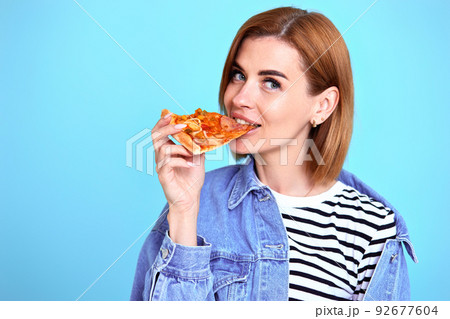 young woman eating pizza slice and looking delighted young woman eating pizza slice and looking delighted 92677604