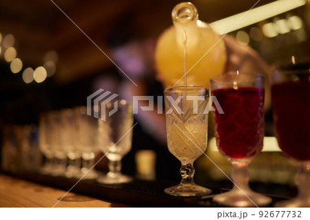 Bartender pouring strong alcoholic drink into small glasses on bar, shots. 92677732