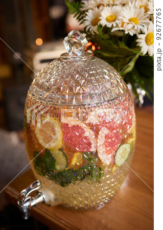 Glass barrel of cold lemonade. Transparent container with tap for soft drinks. Catering services for parties and celebrations. Outdoor bar. 92677765