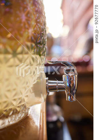 Glass barrel of cold lemonade. Transparent container with tap for soft drinks. Catering services for parties and celebrations. Outdoor bar. 92677770