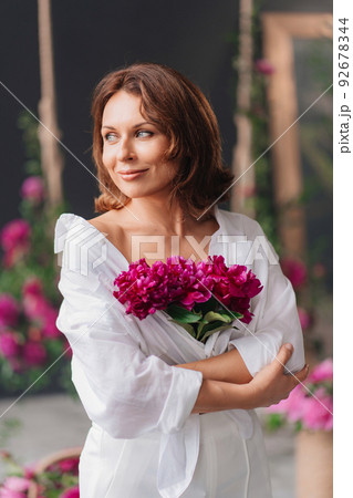 a beautiful middle-aged woman in white clothes with a bouquet of peonies.  92678344